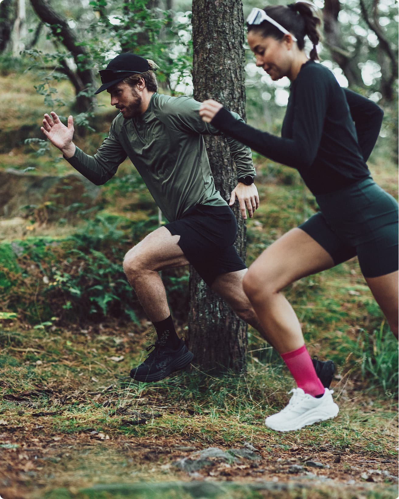 Two people jogging through a forest, dressed in athletic wear. They are mid-stride, surrounded by trees and greenery.
