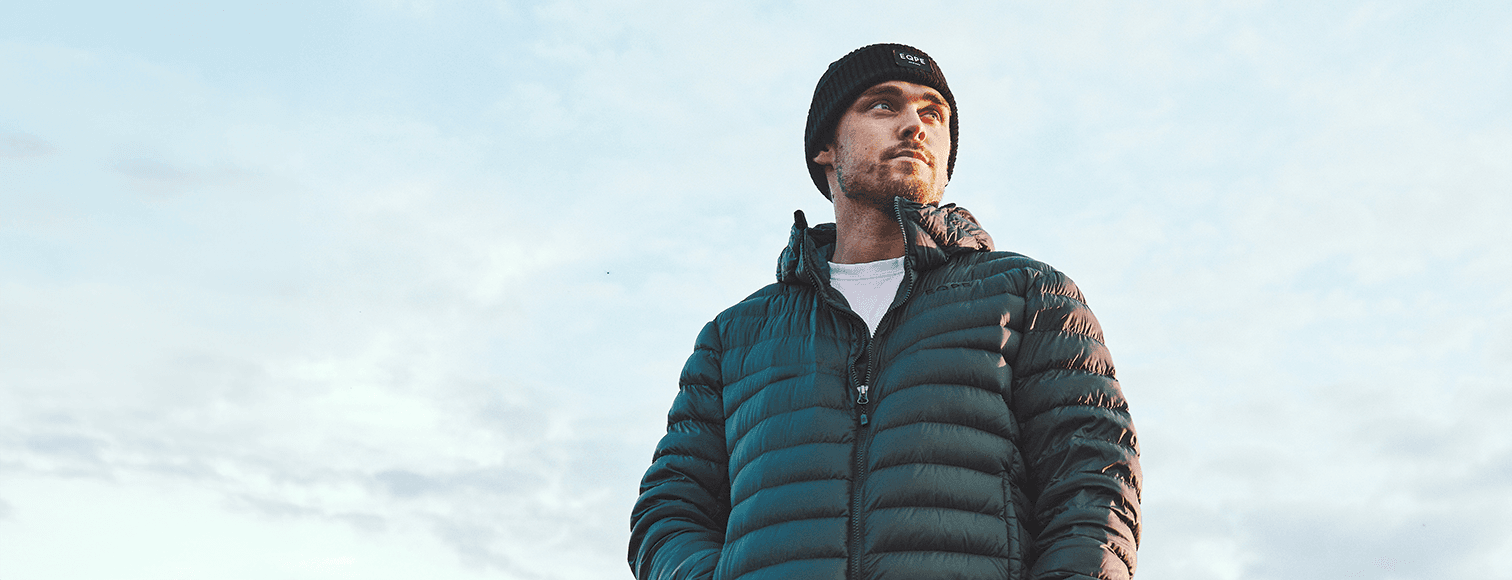 Man in a green liner jacket and black beanie looks into the distance.