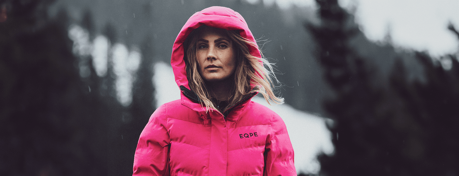 Woman in a bright pink hooded jacket stands outdoors.