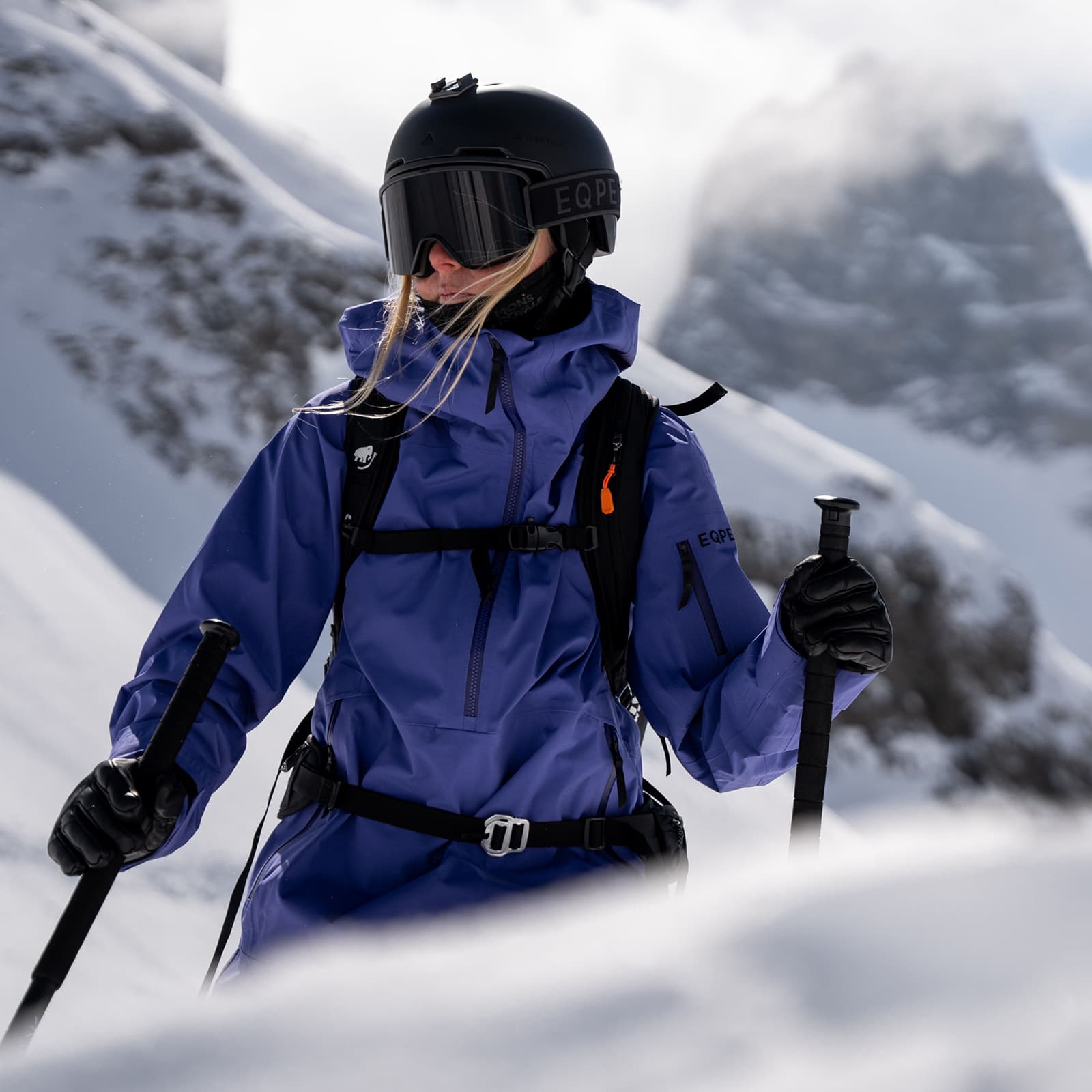 Skier in a purple jacket and black helmet stands on a snowy mountain slope.