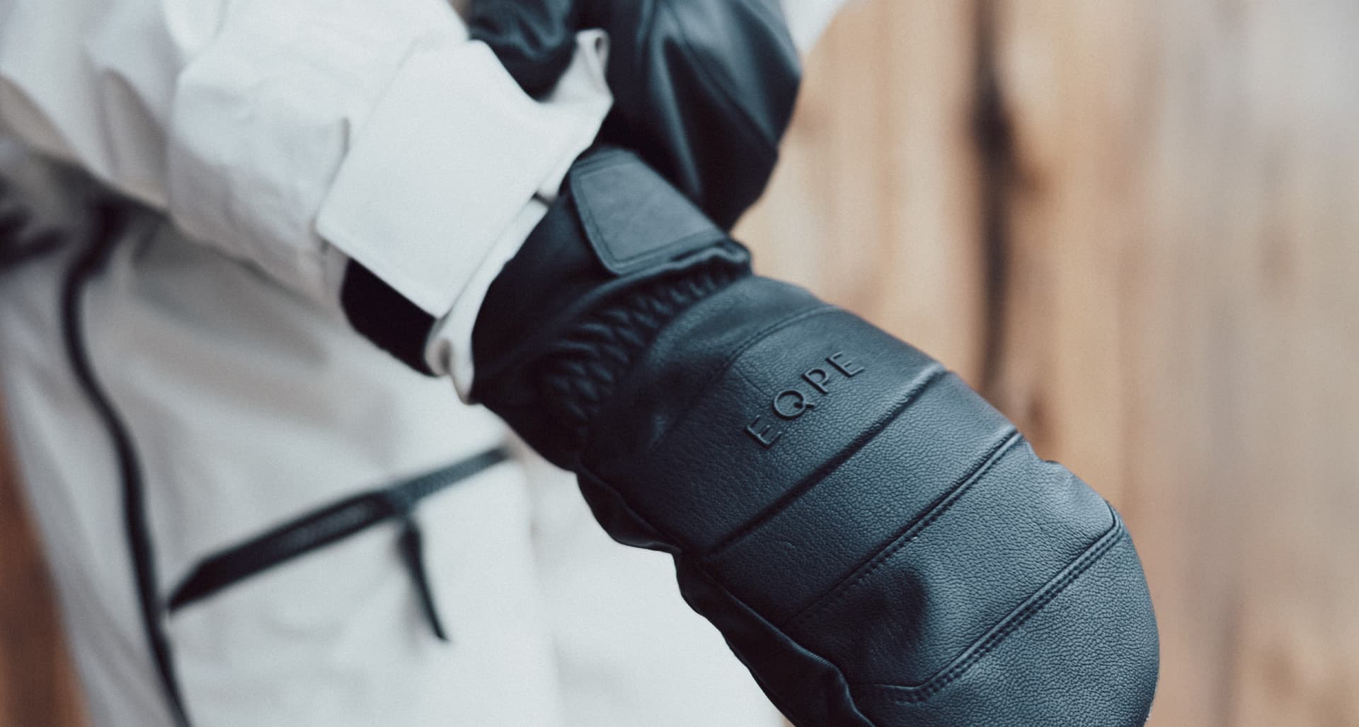 Person wearing black mittens and a white jacket with black accents, extending their arm forward.