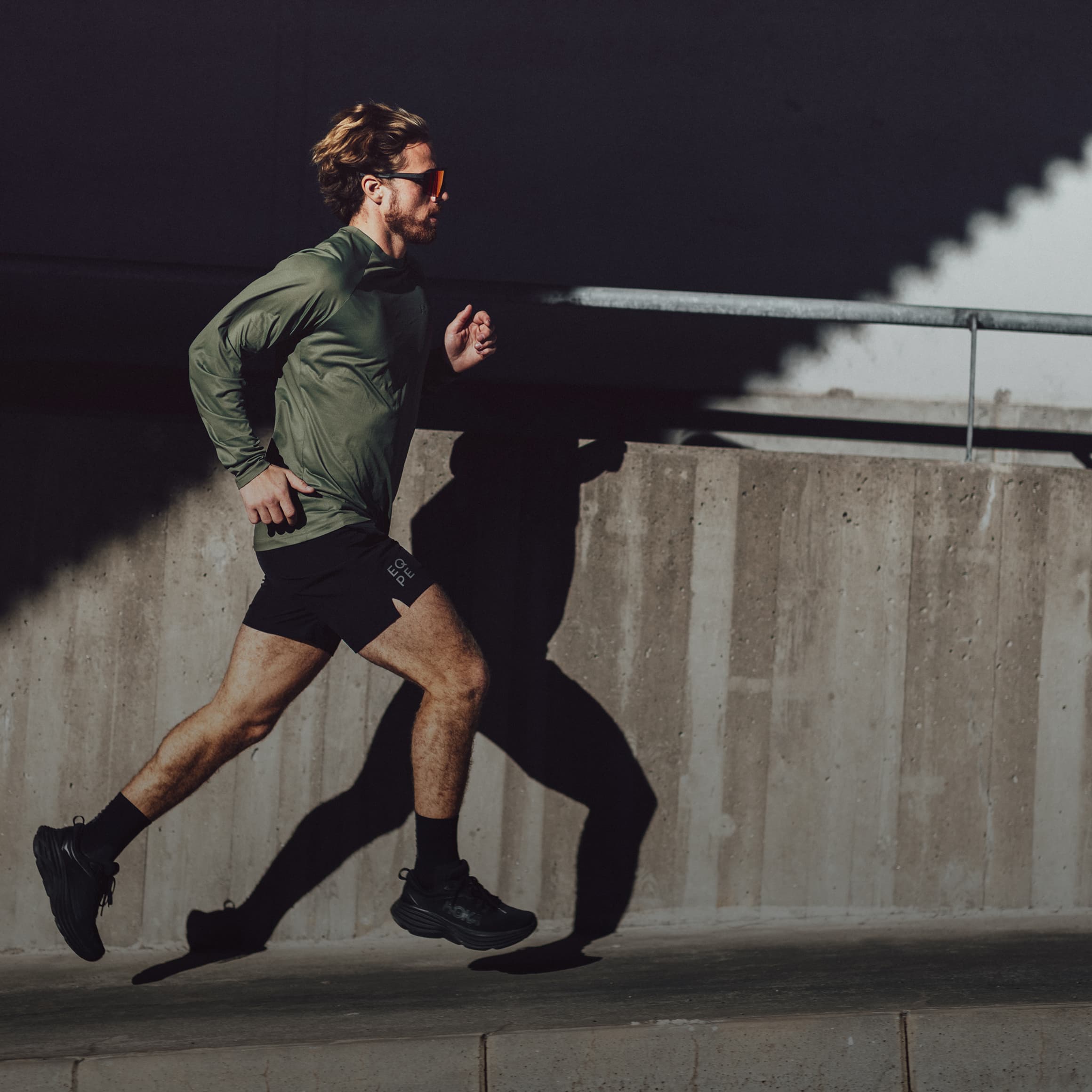 A man runs outdoors, casting a shadow on a concrete wall in bright sunlight.