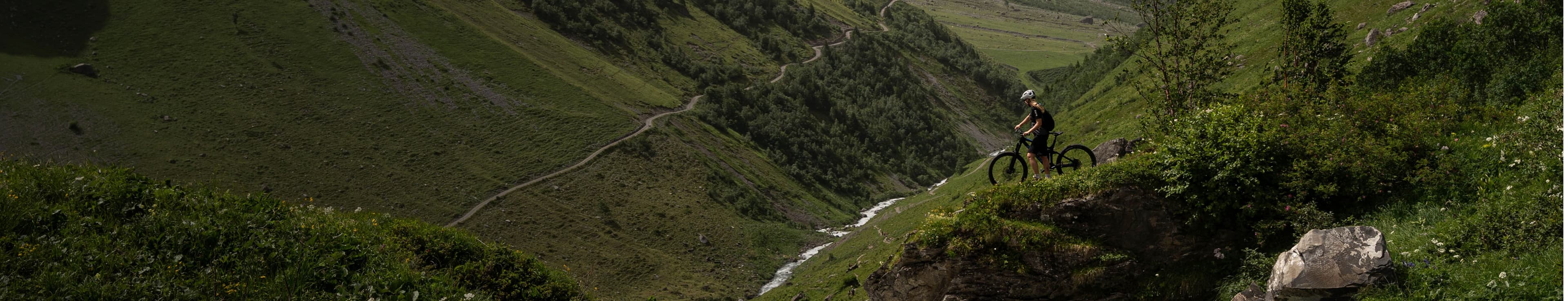 Cyclist on a mountain trail, surrounded by lush green hills.