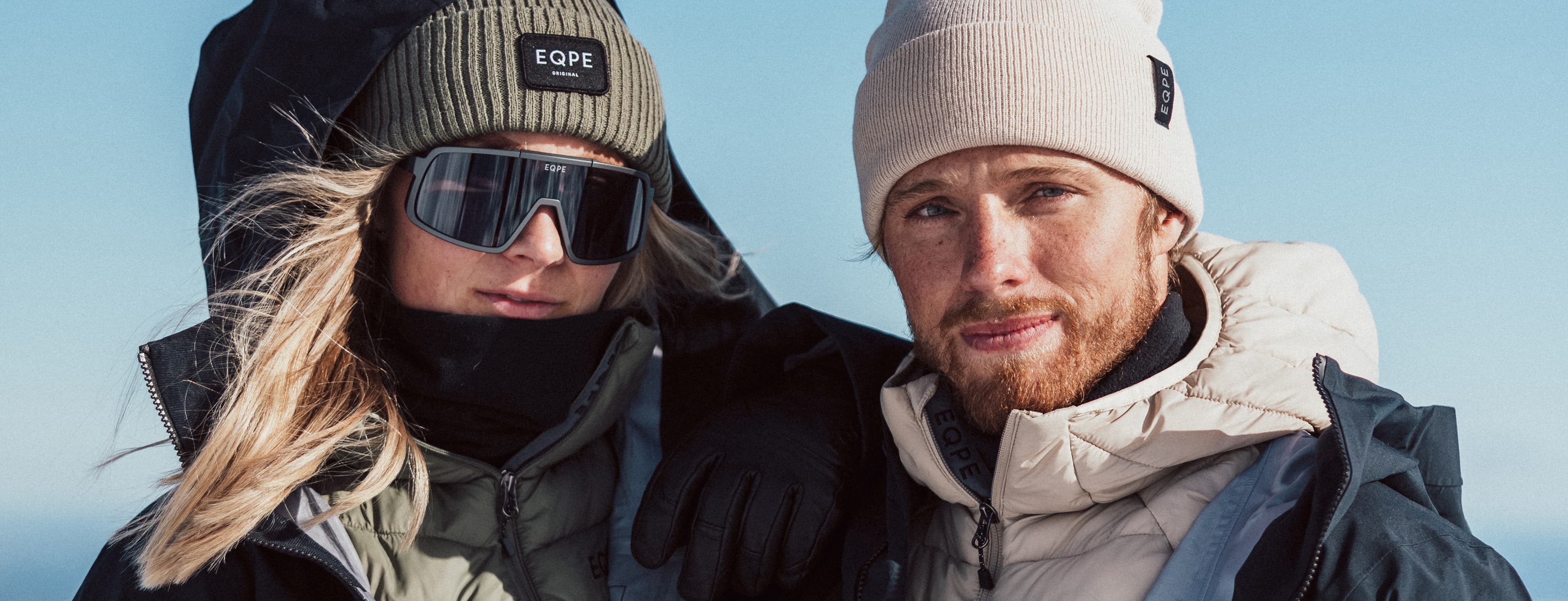 Two people in winter clothing pose against a clear blue sky.